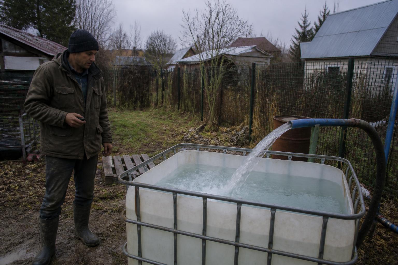 Проверка дебита скважины: вода из шланга льётся в бак, рабочий рядом